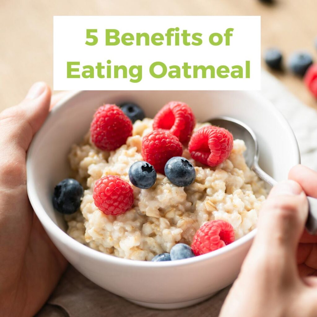hand holding a spoon while eating oatmeal topped with fresh blueberries and raspberries
